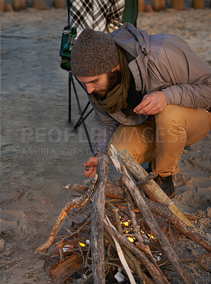 Buy stock photo Campfire, nature and man by beach for travel on vacation, adventure or holiday camping. Wood, outdoor and young male person sitting on chair in sand with flame for heat on weekend trip in winter.
