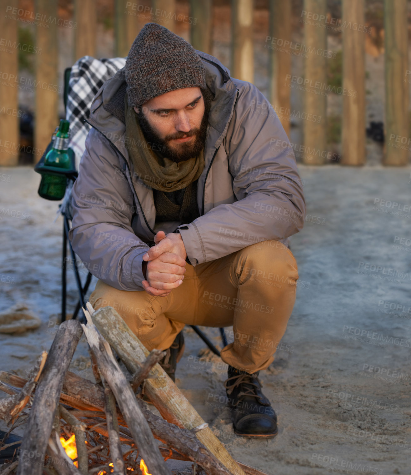 Buy stock photo Campfire, wood and man by beach for travel on vacation, adventure or holiday camping. Nature, outdoor and young male person sitting on chair in sand with flame for heat on weekend trip in winter.
