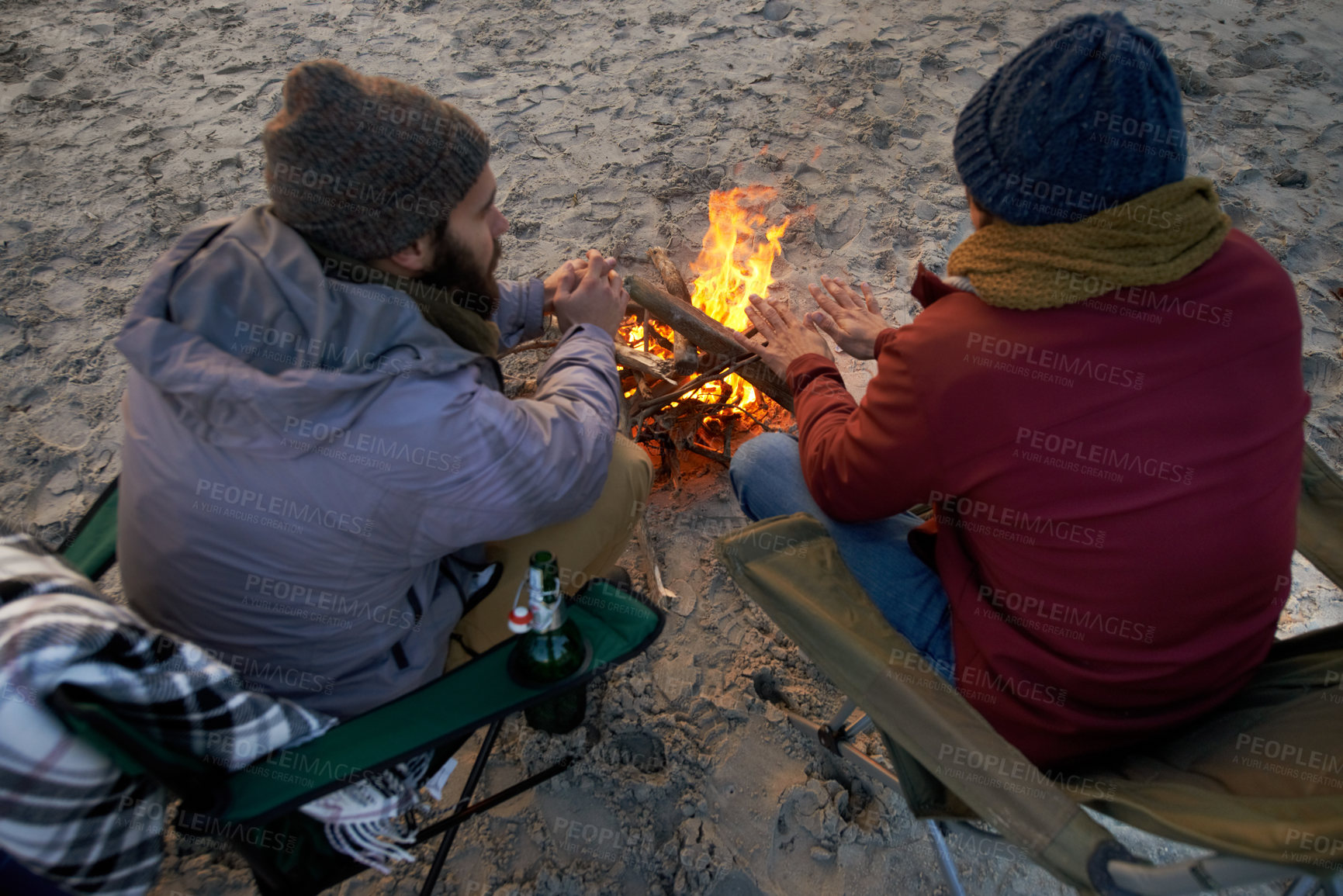 Buy stock photo Campfire, friends and talking with men by the beach at sunset with vacation and camping. Ocean, outdoor and together with travel and people back on trip and journey with fire and conversation by sea