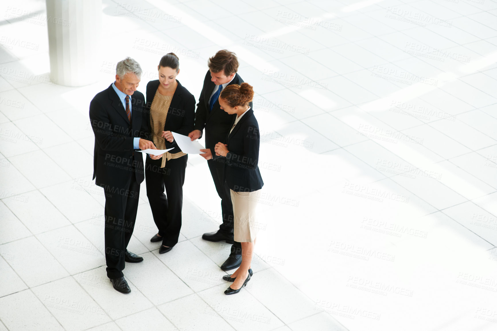 Buy stock photo High-angle view of a group of businesspeople discussing paperwork in an office lobby