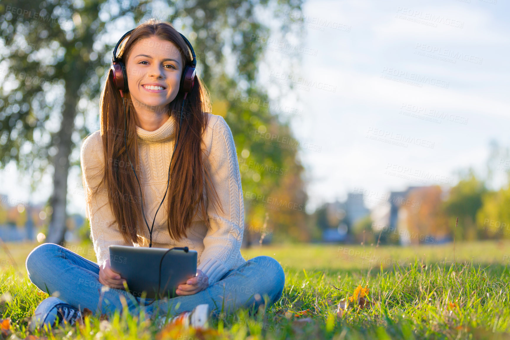 Buy stock photo An attractive young woman listening to music on her digital tablet while outdoors