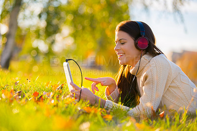 Buy stock photo An attractive young woman listening to music on her digital tablet while outdoors