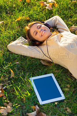 Buy stock photo An attractive young woman listening to music on her digital tablet while outdoors