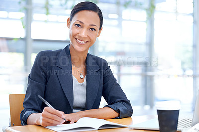 Buy stock photo A businesswoman writing on a notebook while sitting in her office
