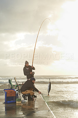 Buy stock photo Fishing, men and net with fish at pier with rod, waves and relax on vacation, holiday and adventure. Friendship, people and bonding in morning with overcast, sky and nature for activity and hobby