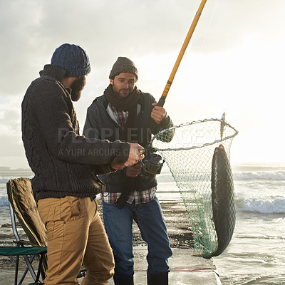 Buy stock photo Fishing, men and net with fish at beach with rod, waves and relax on vacation, holiday and adventure. Friendship, people and bonding in morning with overcast, pier and nature for activity and hobby