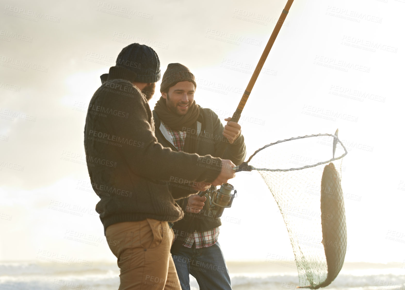 Buy stock photo Fishing, men and net with fish at beach with rod, water and relax on vacation, holiday and travel. Friendship, people and bonding in morning with overcast, sky and nature for activity and hobby