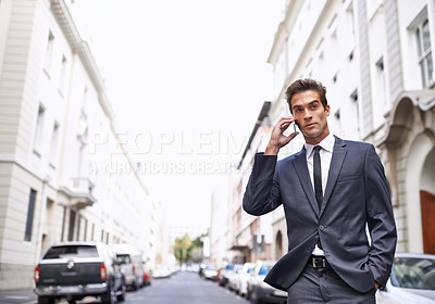 Buy stock photo A handsome businessman in a suit talking on his mobile phone while walking in the city