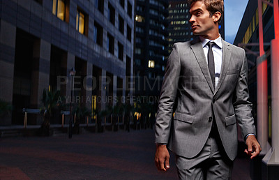 Buy stock photo Shot of a handsome businessman in a suit walking through the city at night