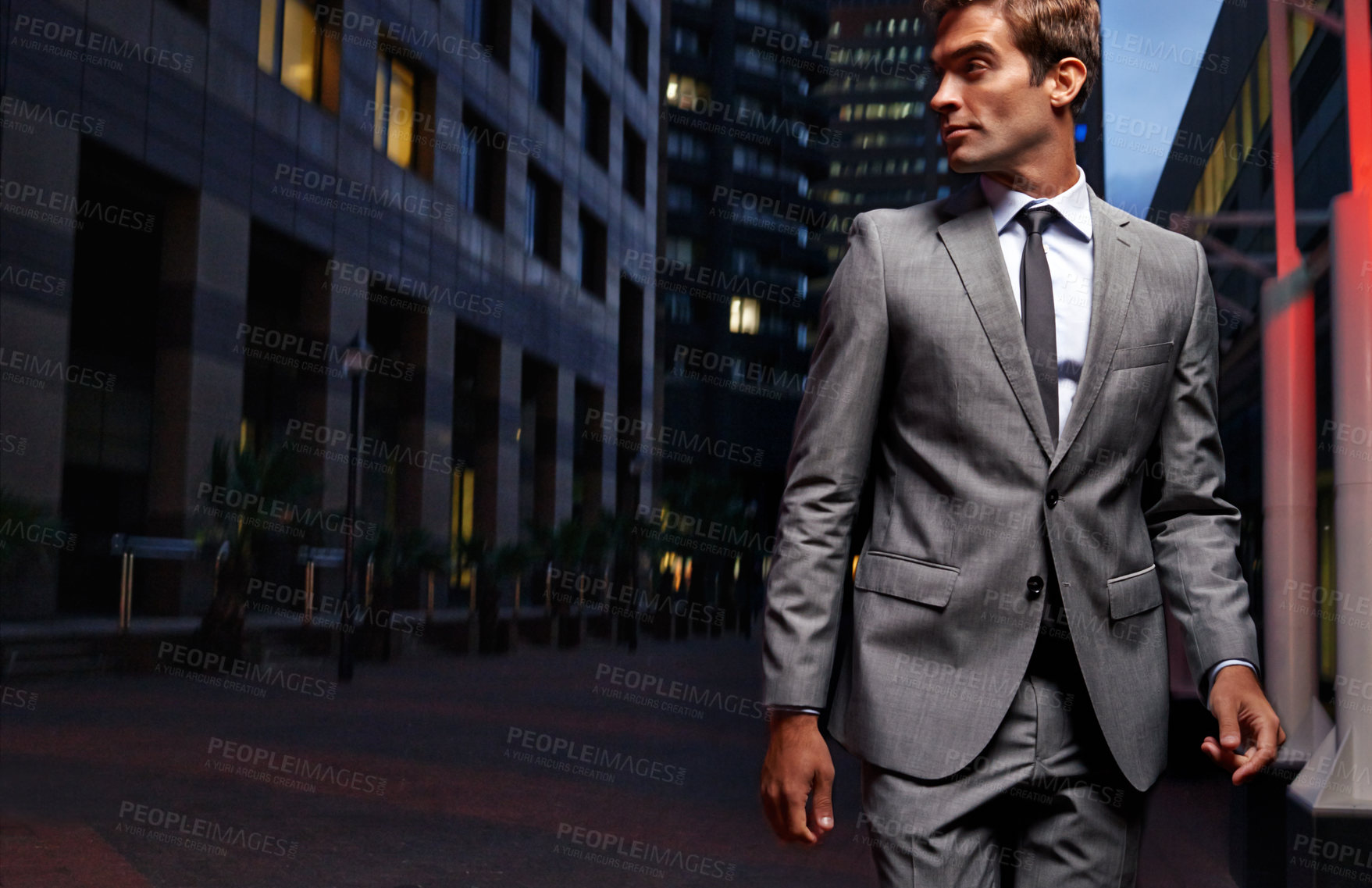 Buy stock photo Shot of a handsome businessman in a suit walking through the city at night