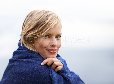 Buy stock photo A young woman sitting by the seaside wrapped in a blanket