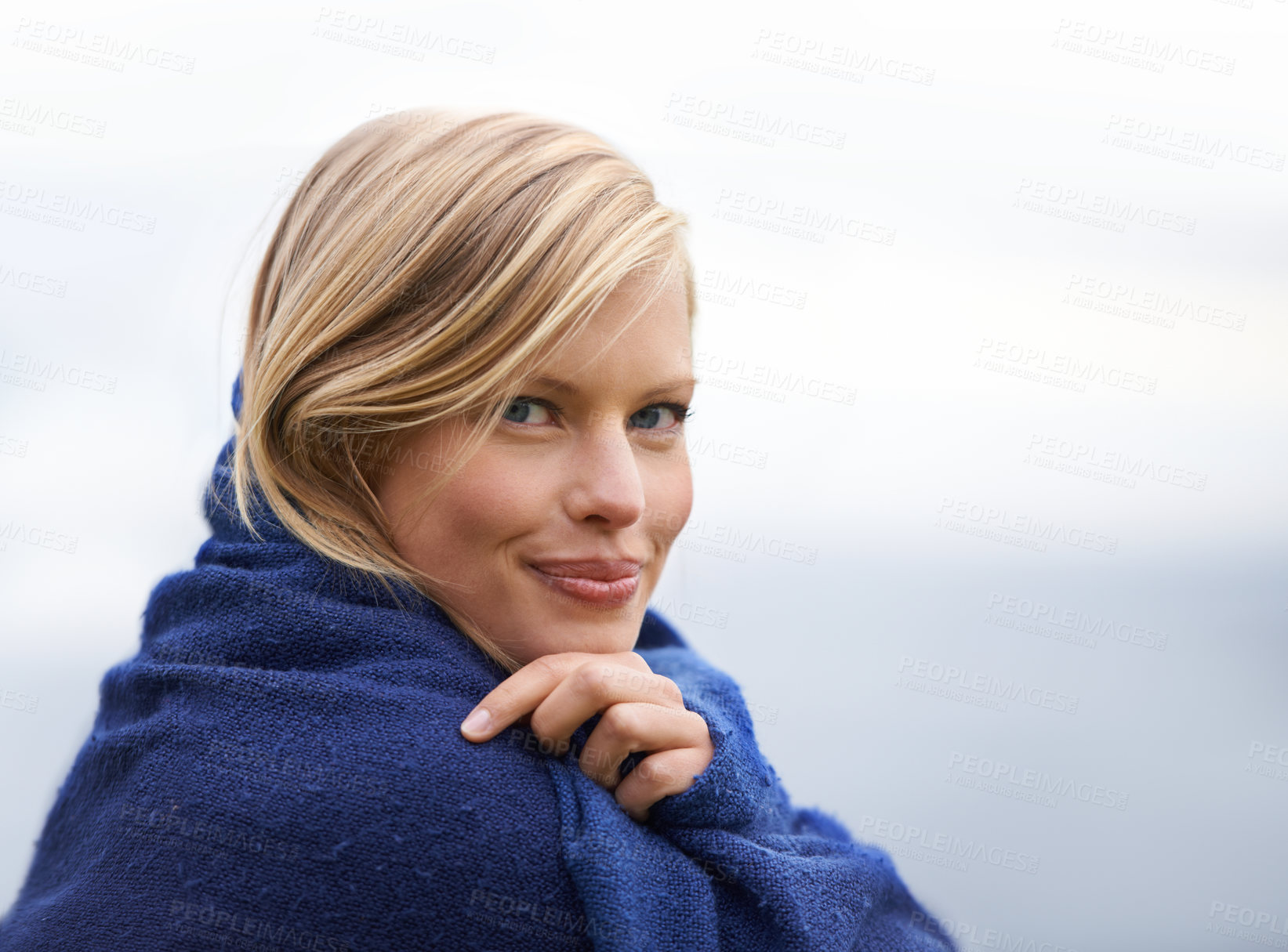 Buy stock photo A young woman sitting by the seaside wrapped in a blanket
