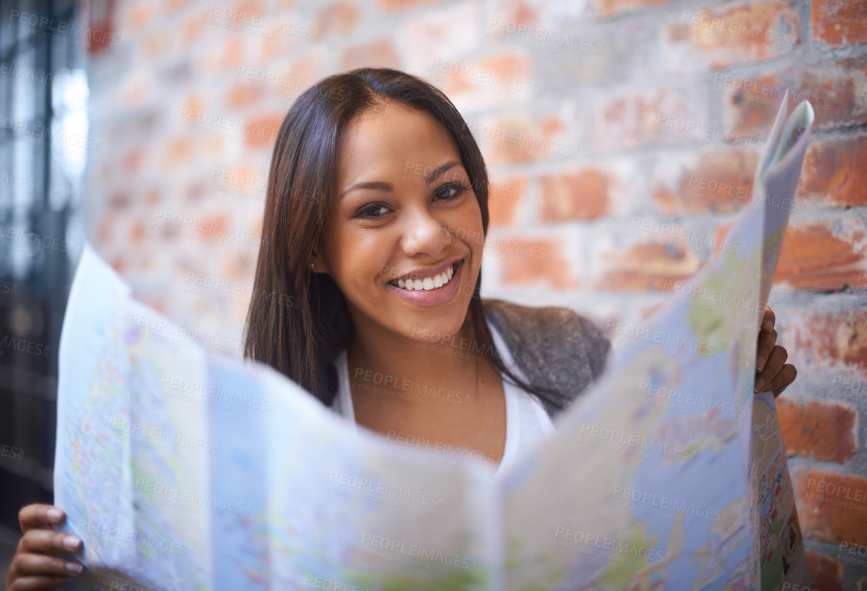 Buy stock photo Happy woman, portrait and reading map for travel, immigration or commute by a brick wall. Face of female person, tourist or traveler with smile for direction, geographic document or world coordinates