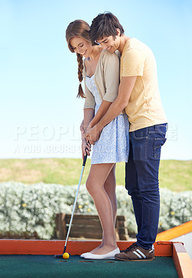 Buy stock photo Young couple, love and outdoor for mini golf in nature, bonding together and happy on weekend with hobby. Man, woman and putt on romantic trip and care, sunshine and teaching girlfriend to play game
