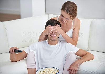 Buy stock photo Couple, popcorn and covered eyes with sofa, surprise and remote for playful movie date. People, living room and film for relaxation, smile and bonding on couch with love and wow at home with break