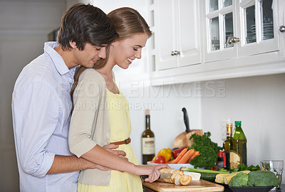 Buy stock photo Shot of a young couple in their kitchen preparing dinner together
