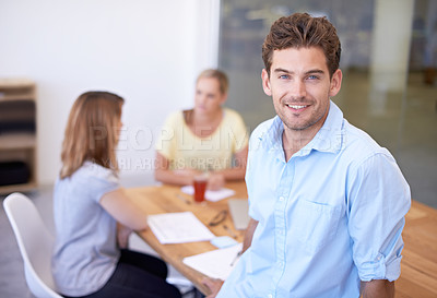 Buy stock photo A handsome young businessman smiling at the camera while his colleagues work in the background