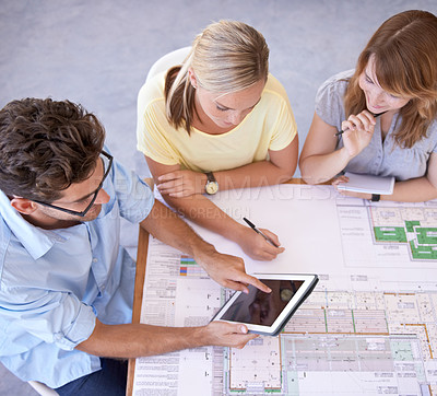 Buy stock photo Shot of a group of young architects using a digital tablet while looking at blueprints