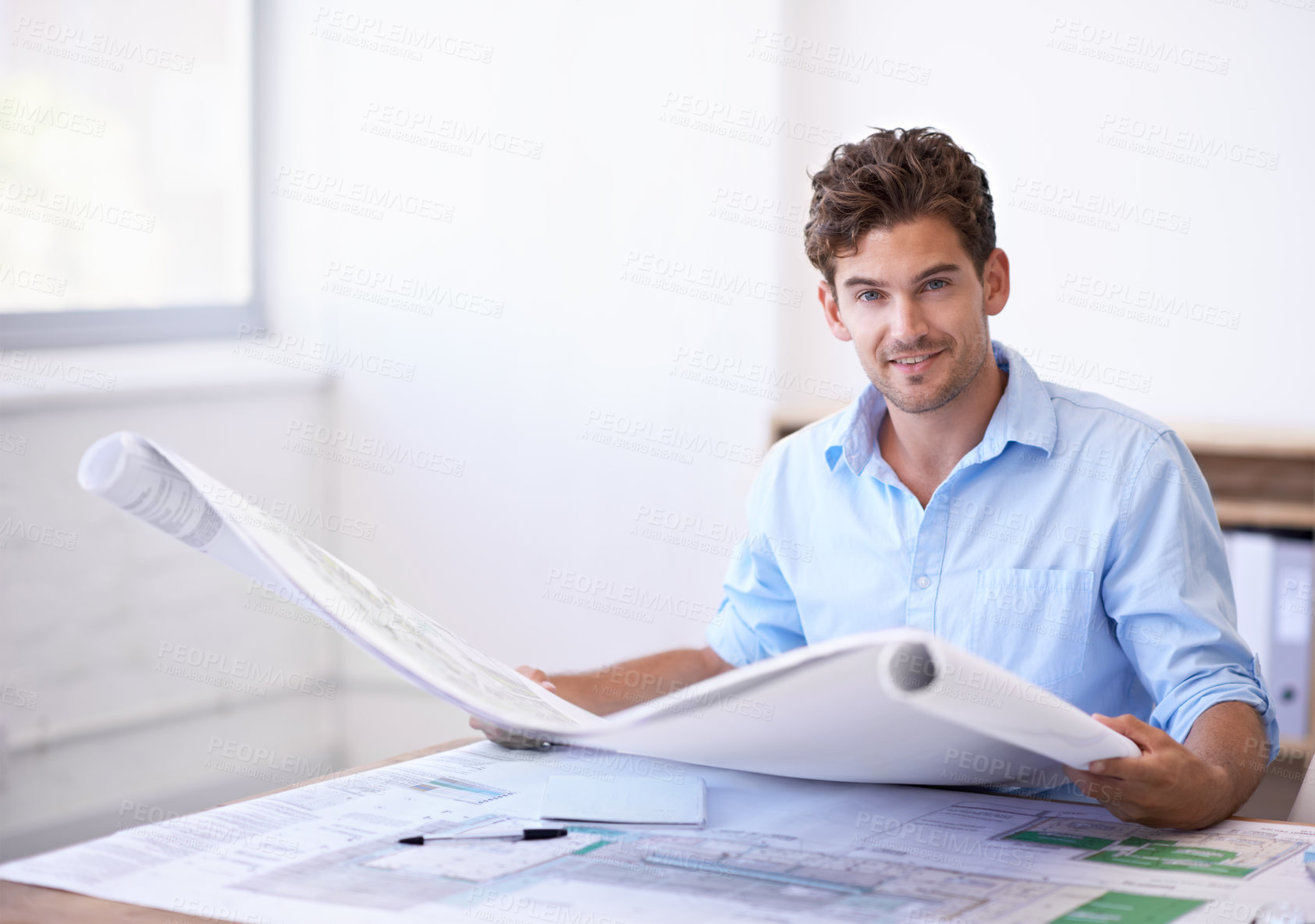 Buy stock photo Shot of an attractive male architect holding plans while sitting in his office