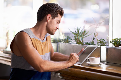 Buy stock photo A young man working on a digital tablet while sitting in a coffee shop