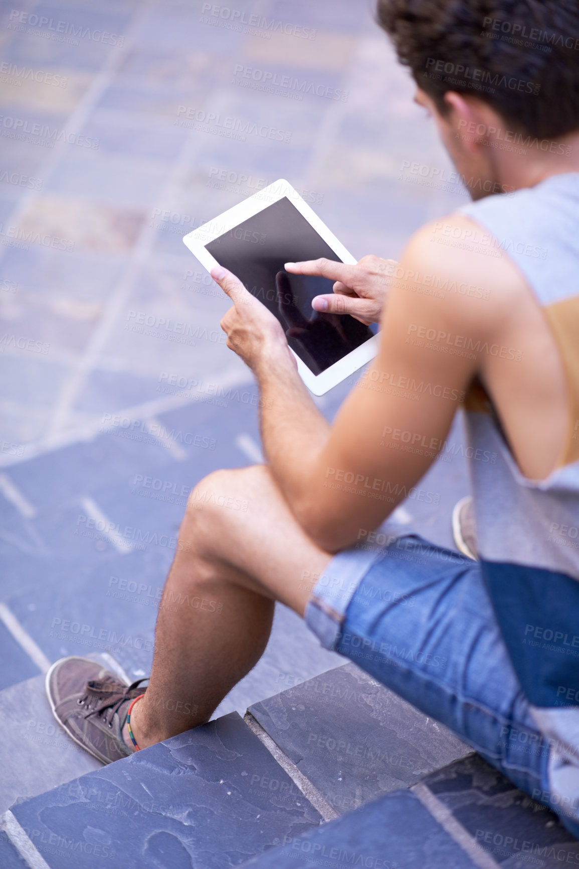 Buy stock photo Over the shoulder shot of a young man sitting on steps using a tablet
