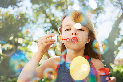 Buy stock photo Shot of a cute young girl blowing bubbles outside