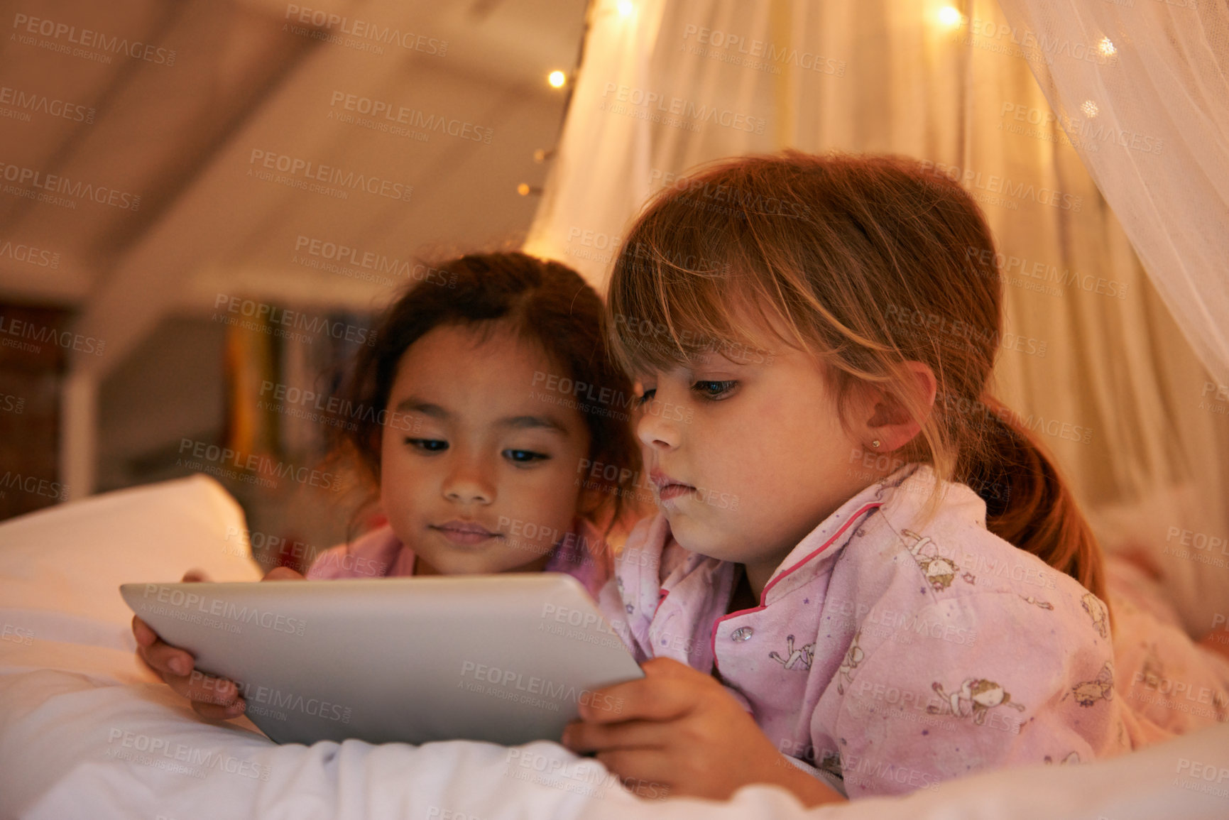 Buy stock photo Girls, tablet or games on bed at night, playing or digital technology for cartoons with love in home. Young kids, friends or connection by fairy light, tent or streaming video for bonding together