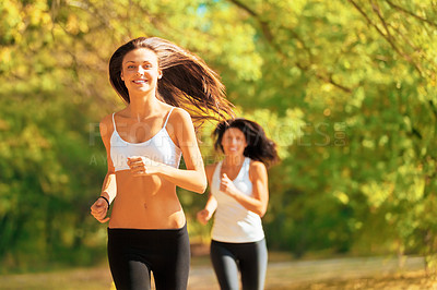 Buy stock photo Shot of two young women jogging together in a park in autumn