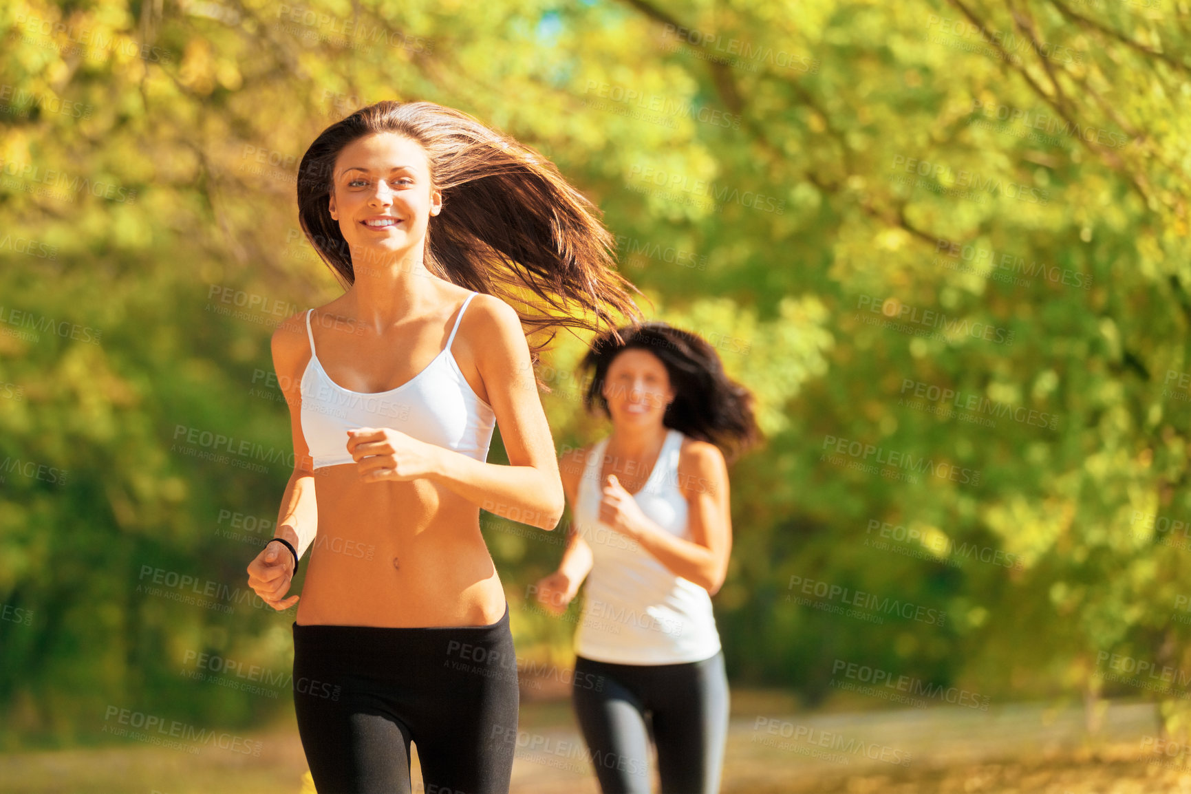 Buy stock photo Shot of two young women jogging together in a park in autumn