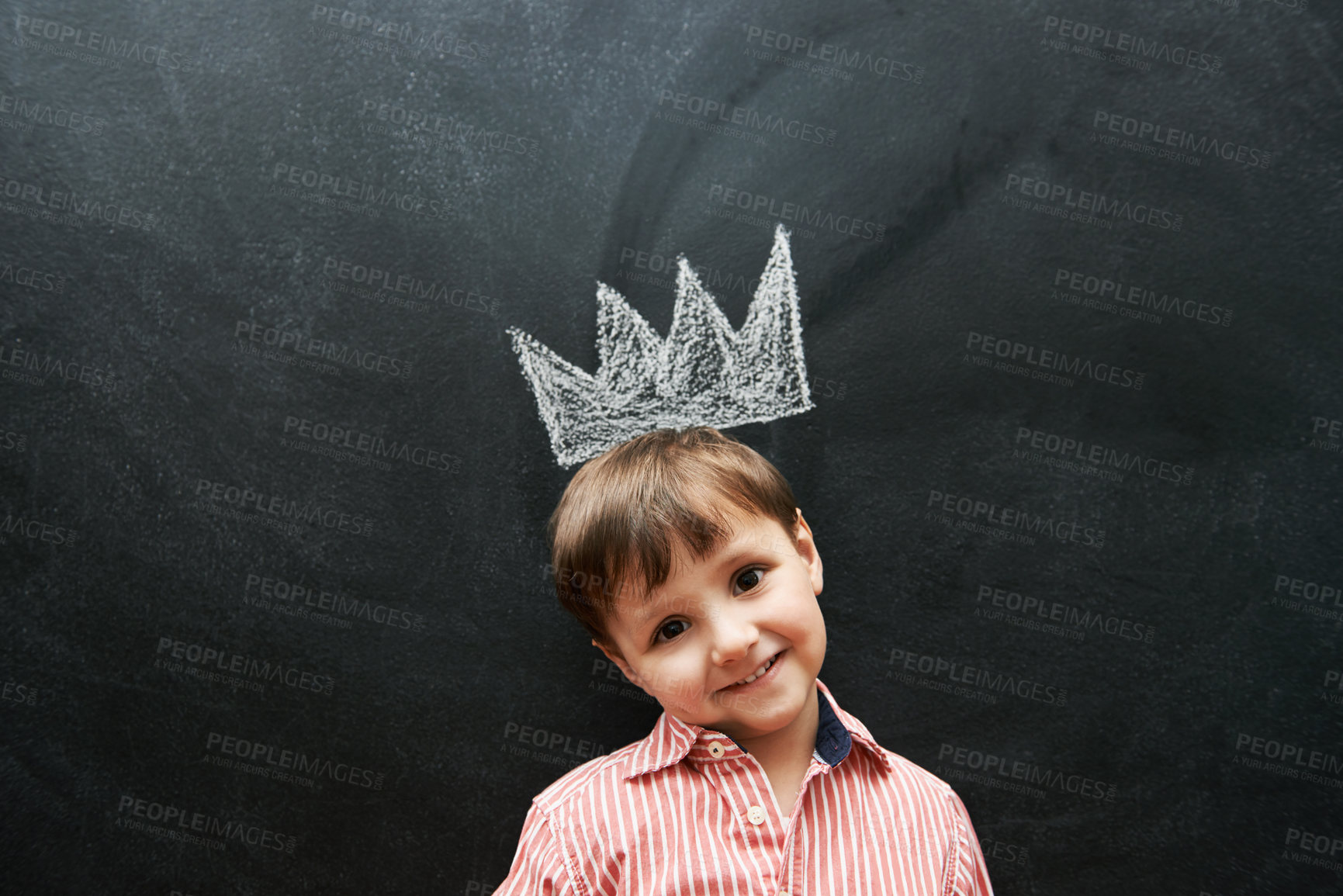 Buy stock photo Little boy, portrait and crown on chalkboard in black background and smile for school in elementary class. Kid, happiness and education for development of learner, blackboard and cute drawing