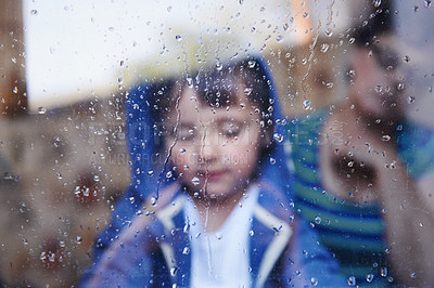 Buy stock photo A little boy looking downwards behind a rain-streaked window while his mother sits in the background