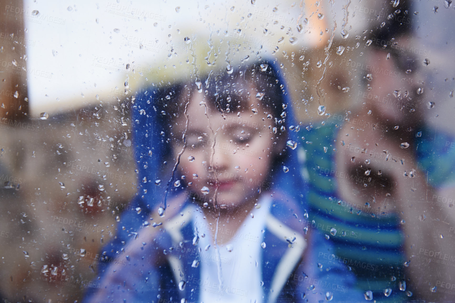 Buy stock photo A little boy looking downwards behind a rain-streaked window while his mother sits in the background