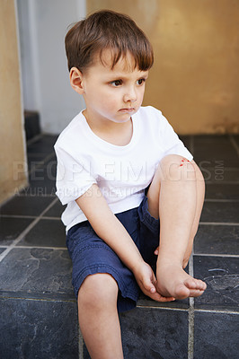 Buy stock photo Little boy, sitting and injury on knee in home and accident, ache and with blood from cut. Young child, sad and holding hurt leg up with hand on foot, pain and sore on bruise with fear of trouble