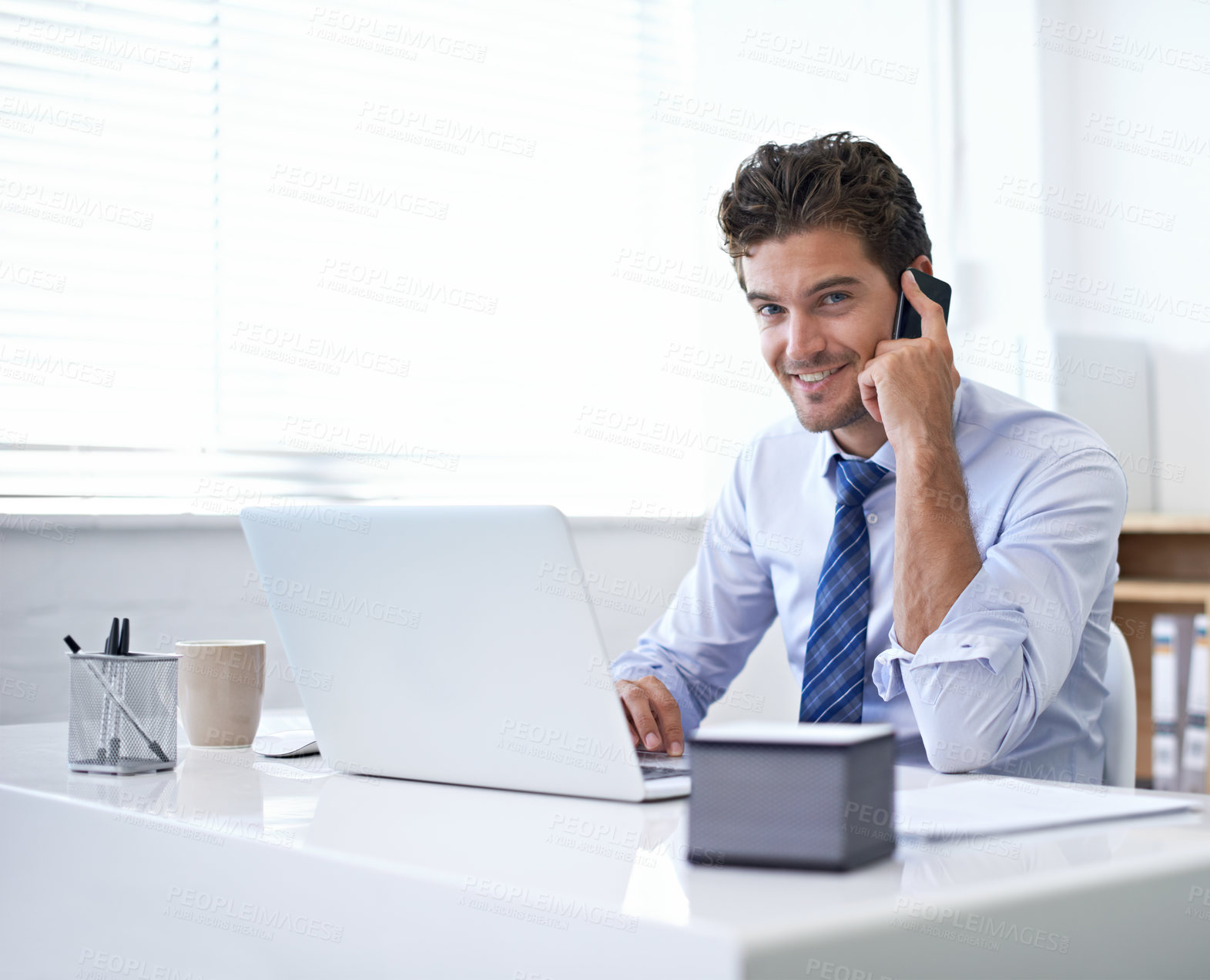 Buy stock photo A young businessman talking on the phone while seated at his desk