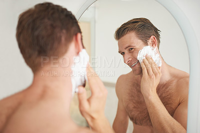 Buy stock photo A handsome young man applying shaving cream to his face in front of a mirror