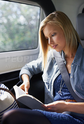 Buy stock photo Shot of a young woman reading a book in the backseat of a car while on a roadtrip