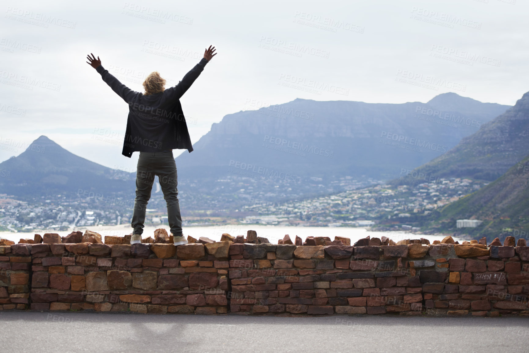 Buy stock photo Person, watching and mountains with arms up in freedom and standing on brick wall in Cape Town. Excited, tourist or traveler with hands in the air for happiness on vacation, holiday or road trip