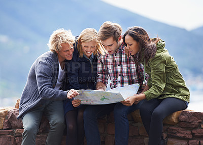 Buy stock photo Shot of a group of friends sitting on a stone wall reading a map