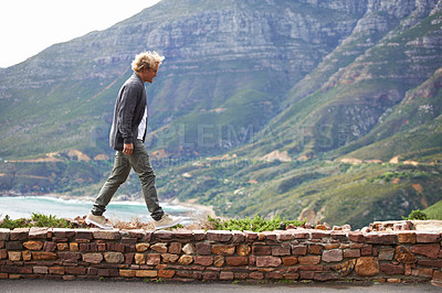 Buy stock photo Travel, man and walking outdoor by mountain on holiday, vacation or trekking on trip in South Africa. Ocean, sea and person by stone wall for adventure, journey or tourist explore nature for hiking