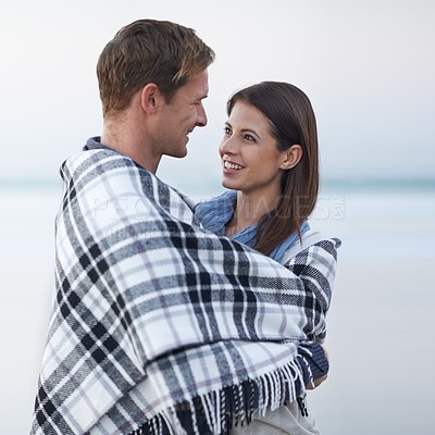 Buy stock photo Couple, hug and smile at beach with blanket for vacation, love and care on date at sunset by ocean. Man, woman and embrace with break, bonding and travel for memory on holiday by sea in Australia