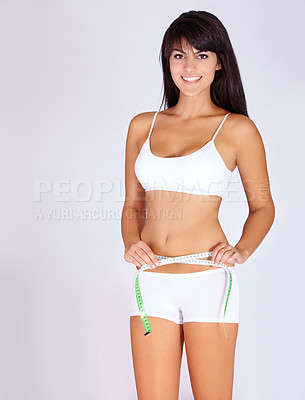 Buy stock photo Studio portrait of an attractive young woman measuring her waist