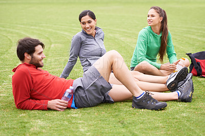 Buy stock photo Shot of a group of young people relaxing on the grass after exercising