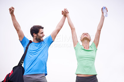 Buy stock photo A young couple in sportswear raising their hands in the air as they celebrate a victory