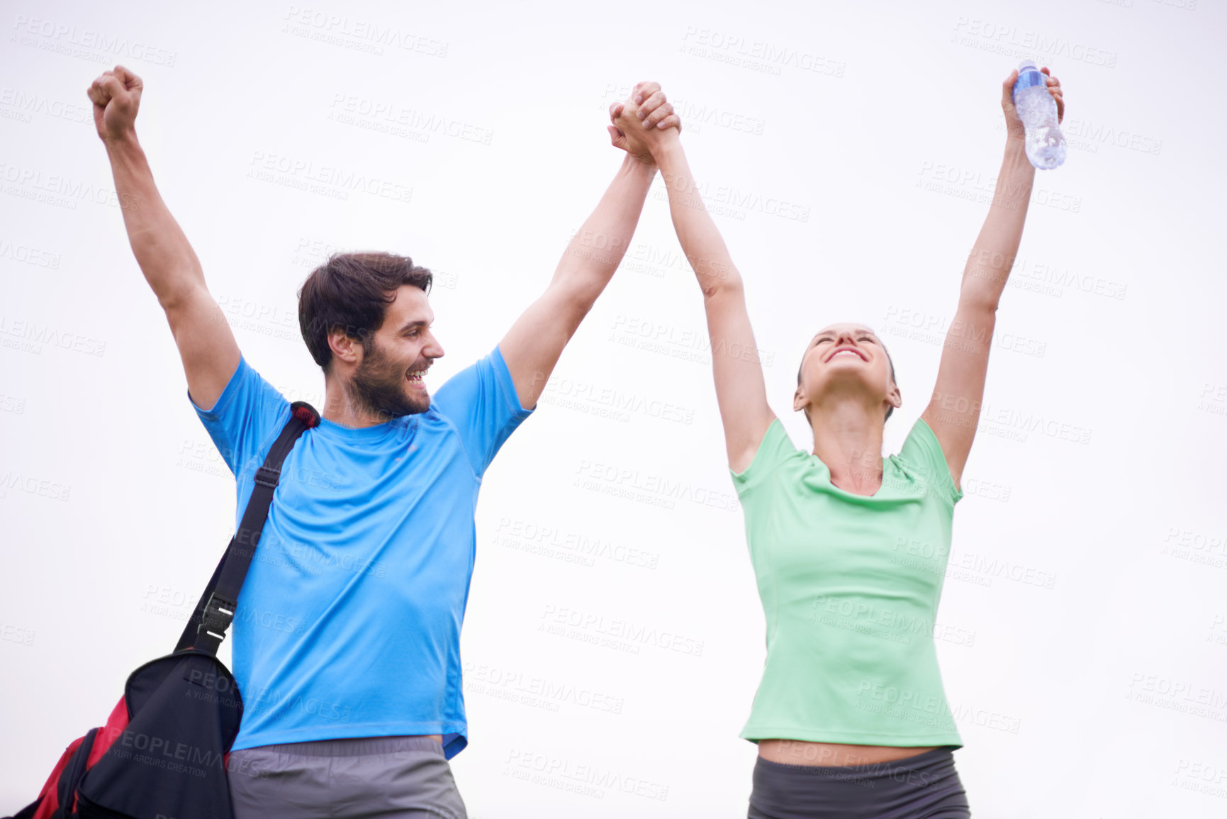Buy stock photo A young couple in sportswear raising their hands in the air as they celebrate a victory