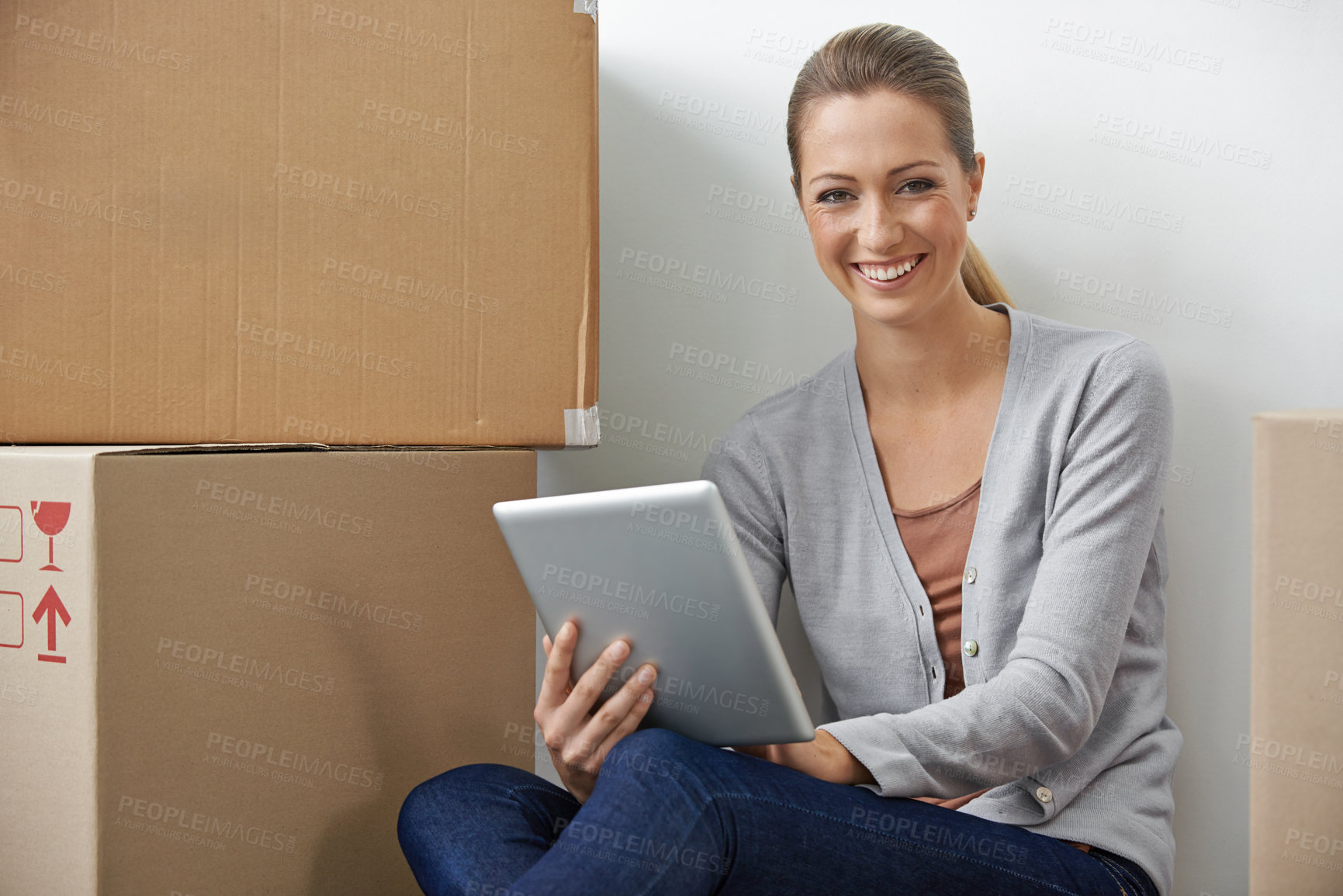 Buy stock photo A young woman working on her digital tablet while sitting next to boxes