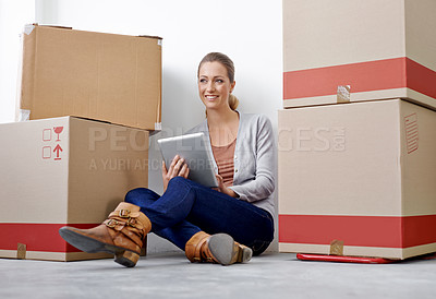 Buy stock photo A young woman working on her digital tablet while sitting amongst boxes in an office