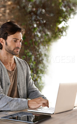 Buy stock photo A handsome young man working on his laptop outdoors