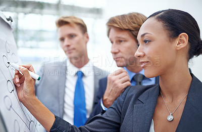 Buy stock photo A businesswoman drawing a diagram on a flip-chart as her colleagues stand by