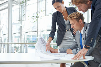 Buy stock photo Shot of three design professionals looking over some plans