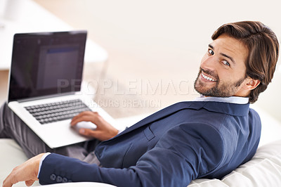 Buy stock photo An attractive businessman reclining on the couch while working on his laptop